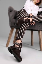 Young stylish woman with trendy shoes sitting in armchair on grey background