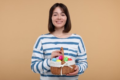 Photo of Easter celebration. Happy woman with wicker basket full of painted eggs on beige background