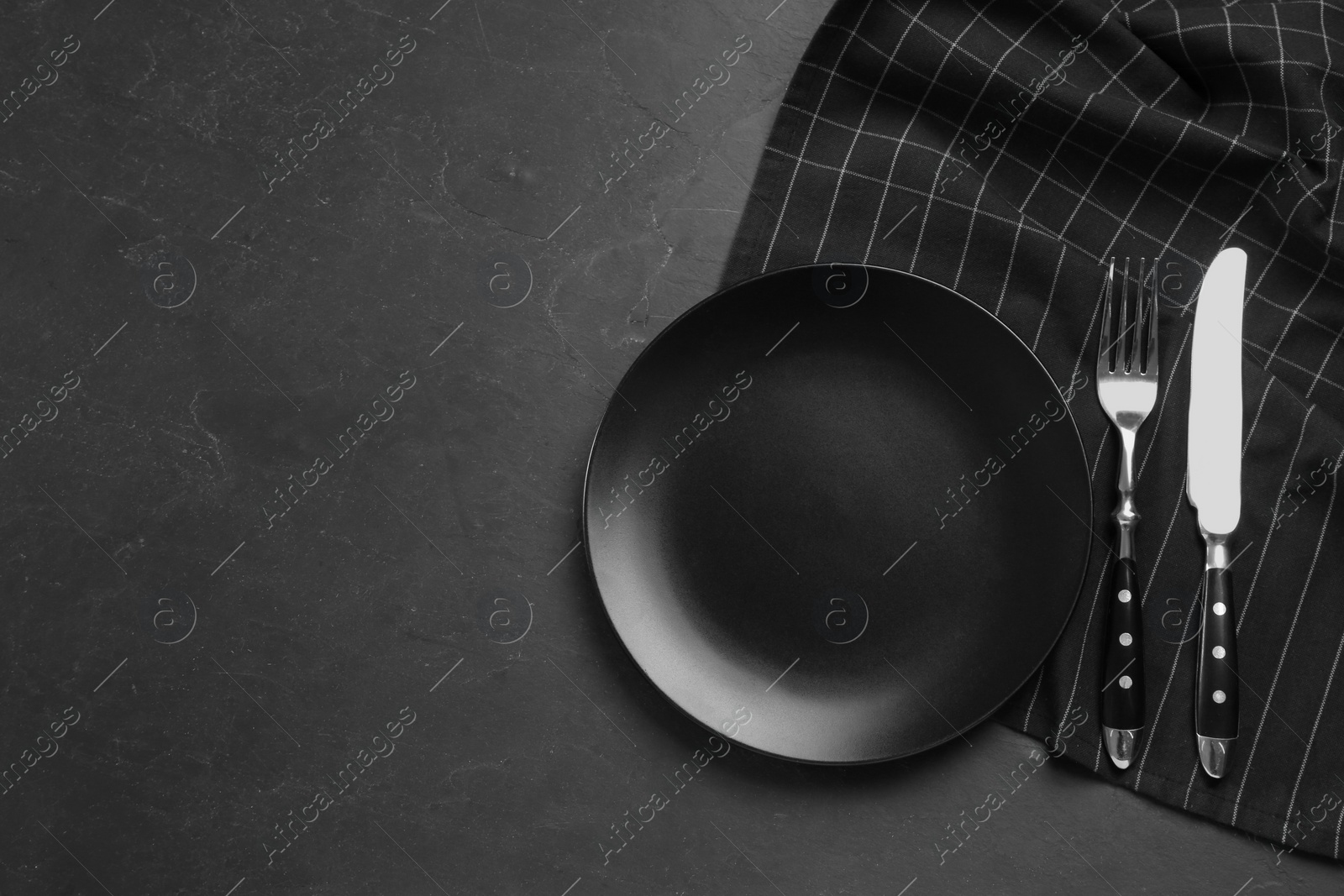 Photo of Ceramic plate, fork and knife on black table, flat lay. Space for text