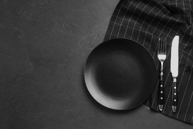 Ceramic plate, fork and knife on black table, flat lay. Space for text