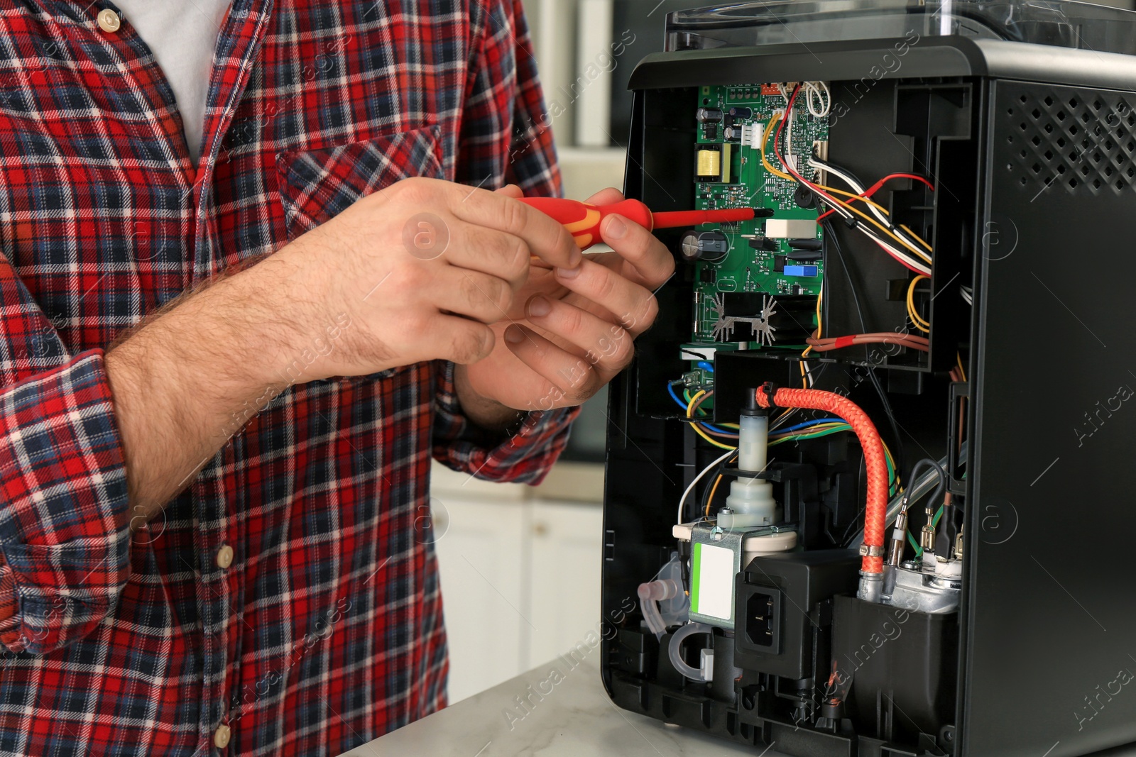 Photo of Man with screwdriver fixing coffee machine at table indoors, closeup