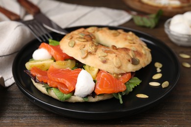 Tasty bagel with salmon, mozzarella cheese, tomatoes and lettuce on wooden table, closeup