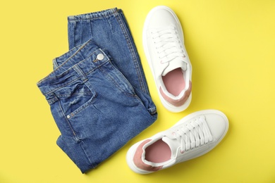 Photo of Stylish white sneakers and jeans on yellow background, flat lay