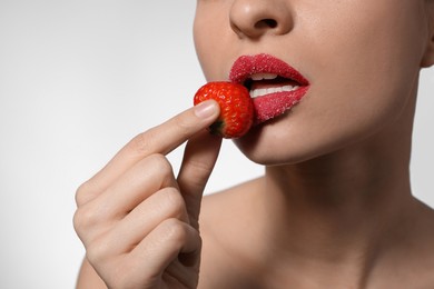 Photo of Young woman with lips covered in sugar holding strawberry on light background, closeup
