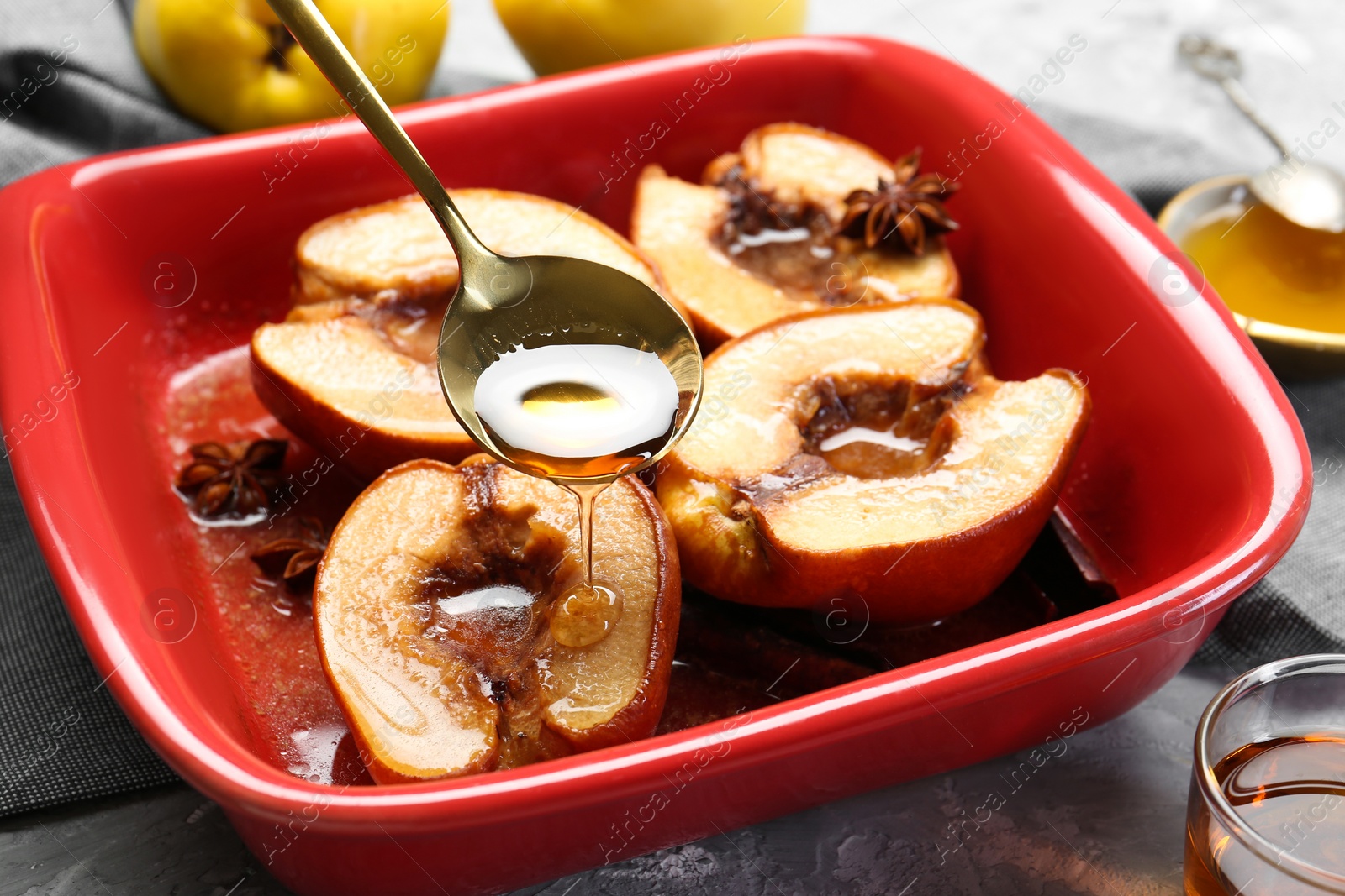 Photo of Pouring tasty honey onto baked quinces in dish on grey textured table, closeup