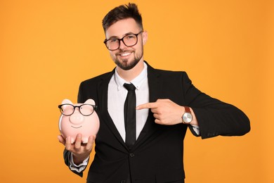 Photo of Happy businessman with piggy bank on orange background