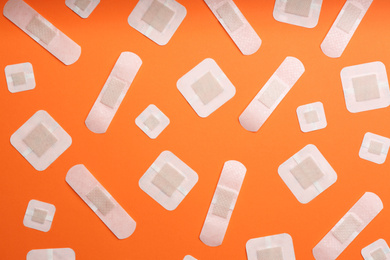 Photo of Different types of sticking plasters on orange background, flat lay