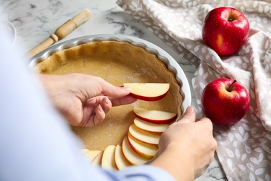 Woman putting apple slice into baking dish with dough to make traditional English pie at white marble table, closeup