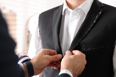 Photo of Professional tailor working with client in atelier, closeup