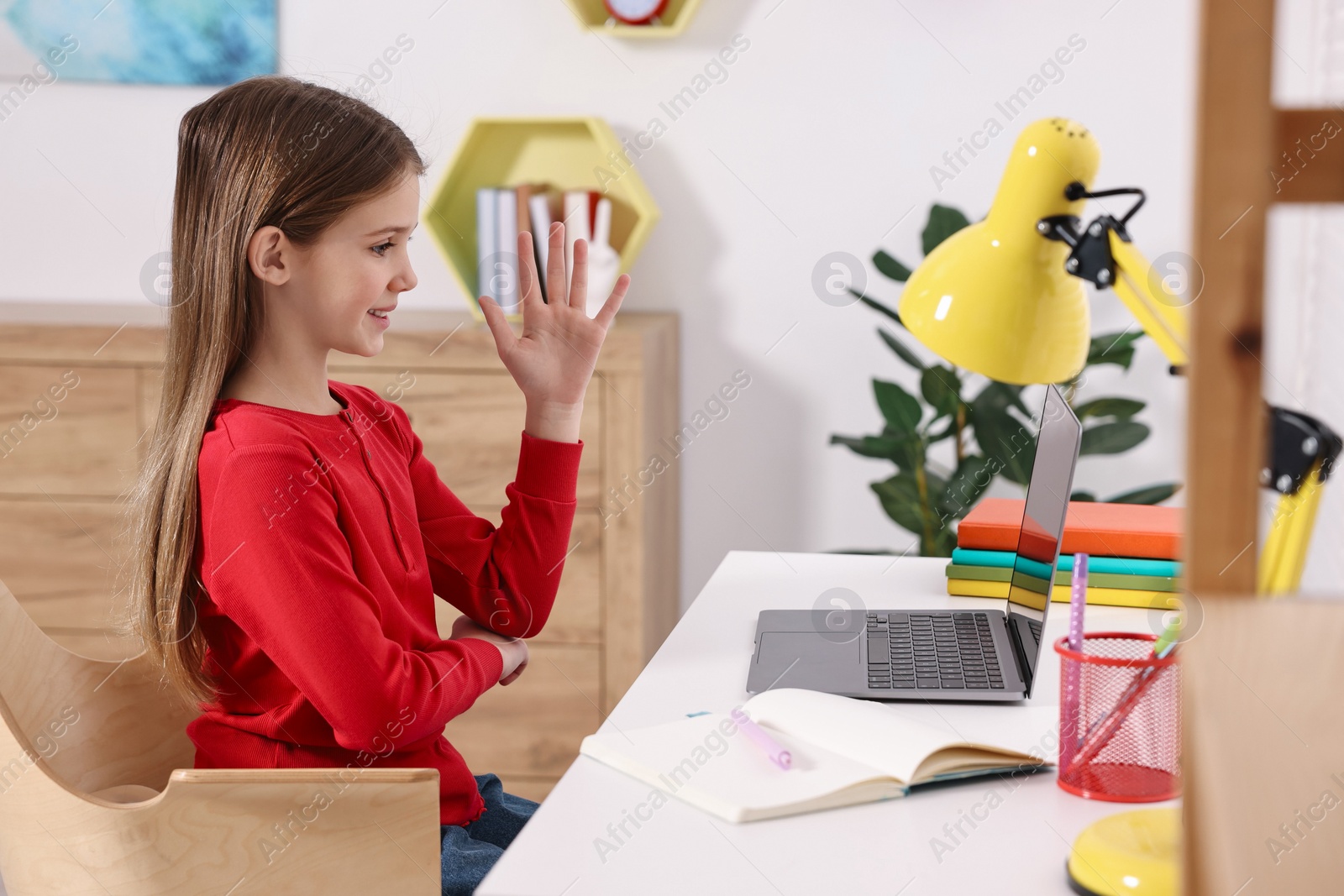 Photo of E-learning. Cute girl raising her hand to answer during online lesson at table indoors