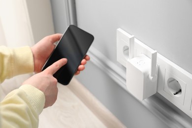 Woman using smartphone for wireless Wi-Fi repeater indoors, closeup