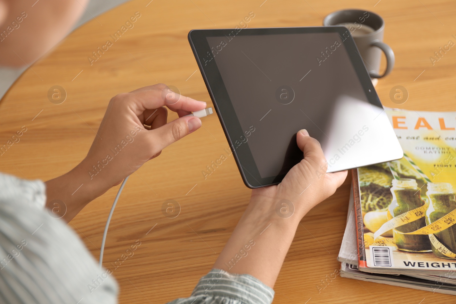 Photo of Woman connecting charger cable to tablet at wooden table, closeup