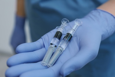 Doctor holding syringes with COVID-19 vaccine, closeup