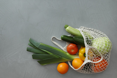Net bag with fruits and vegetables on light grey table, flat lay