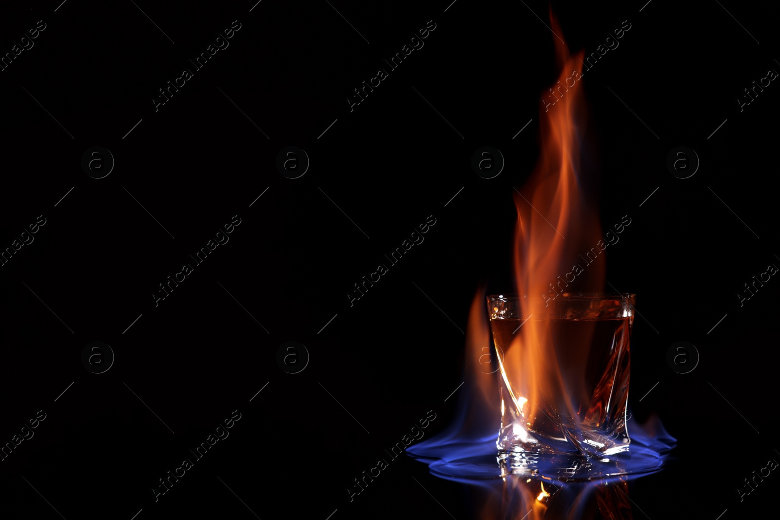 Photo of Glass with flaming vodka on black background, space for text