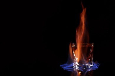 Photo of Glass with flaming vodka on black background, space for text