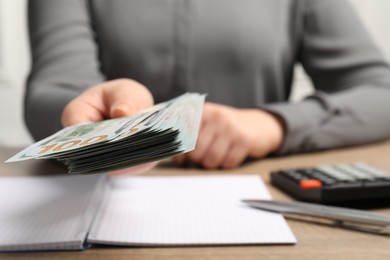 Photo of Money exchange. Woman holding dollar banknotes at wooden table, closeup