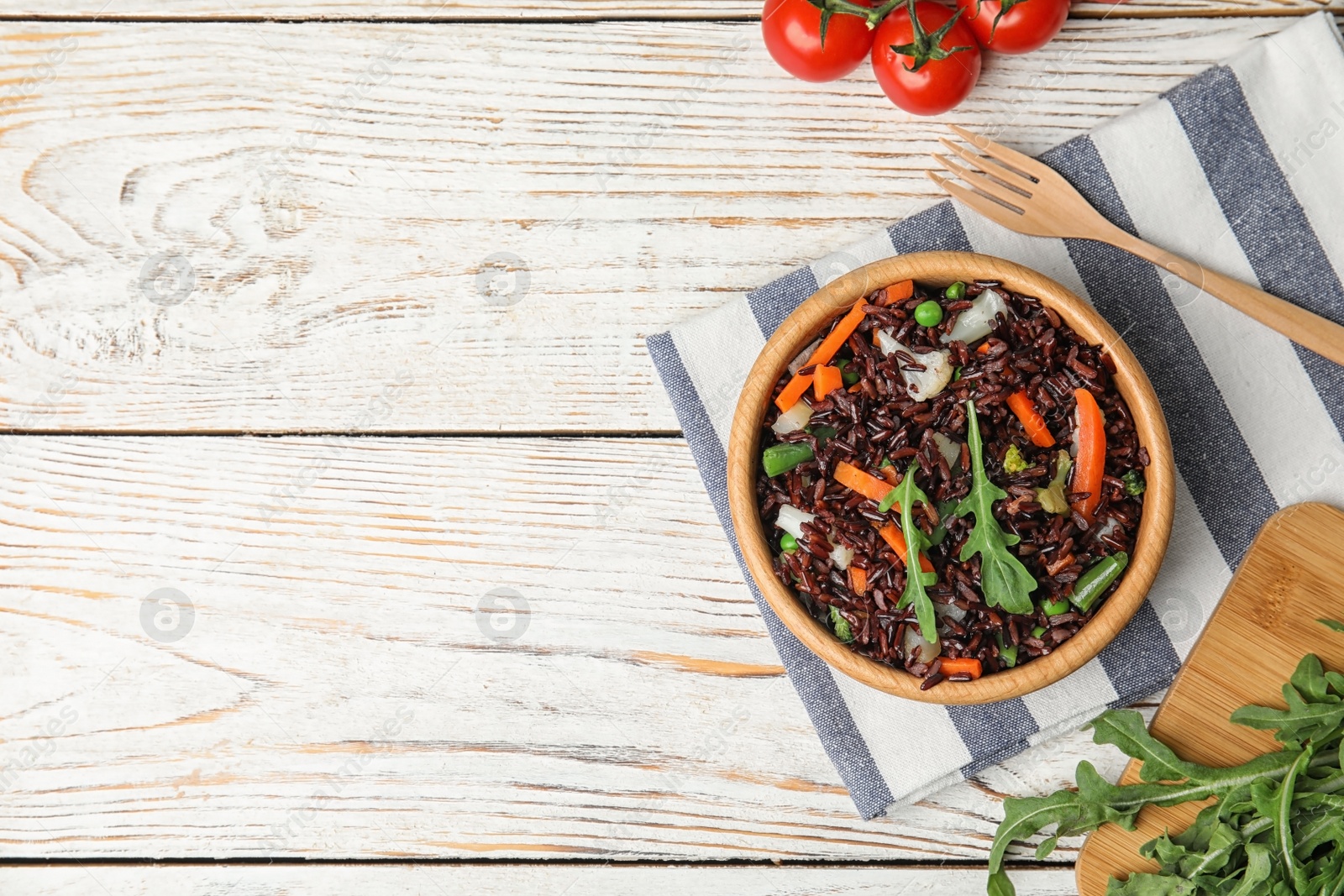 Photo of Bowl of brown rice with vegetables on light wooden table, flat lay. Space for text