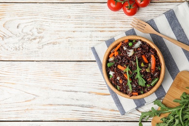 Photo of Bowl of brown rice with vegetables on light wooden table, flat lay. Space for text