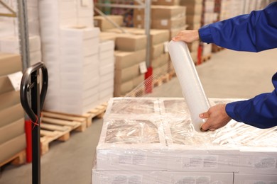 Photo of Worker wrapping boxes in stretch film at warehouse, closeup