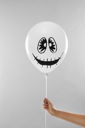 Photo of Woman holding spooky balloon for Halloween party on light grey background, closeup