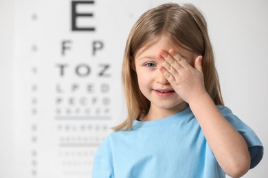 Photo of Little girl covering her eye against vision test chart