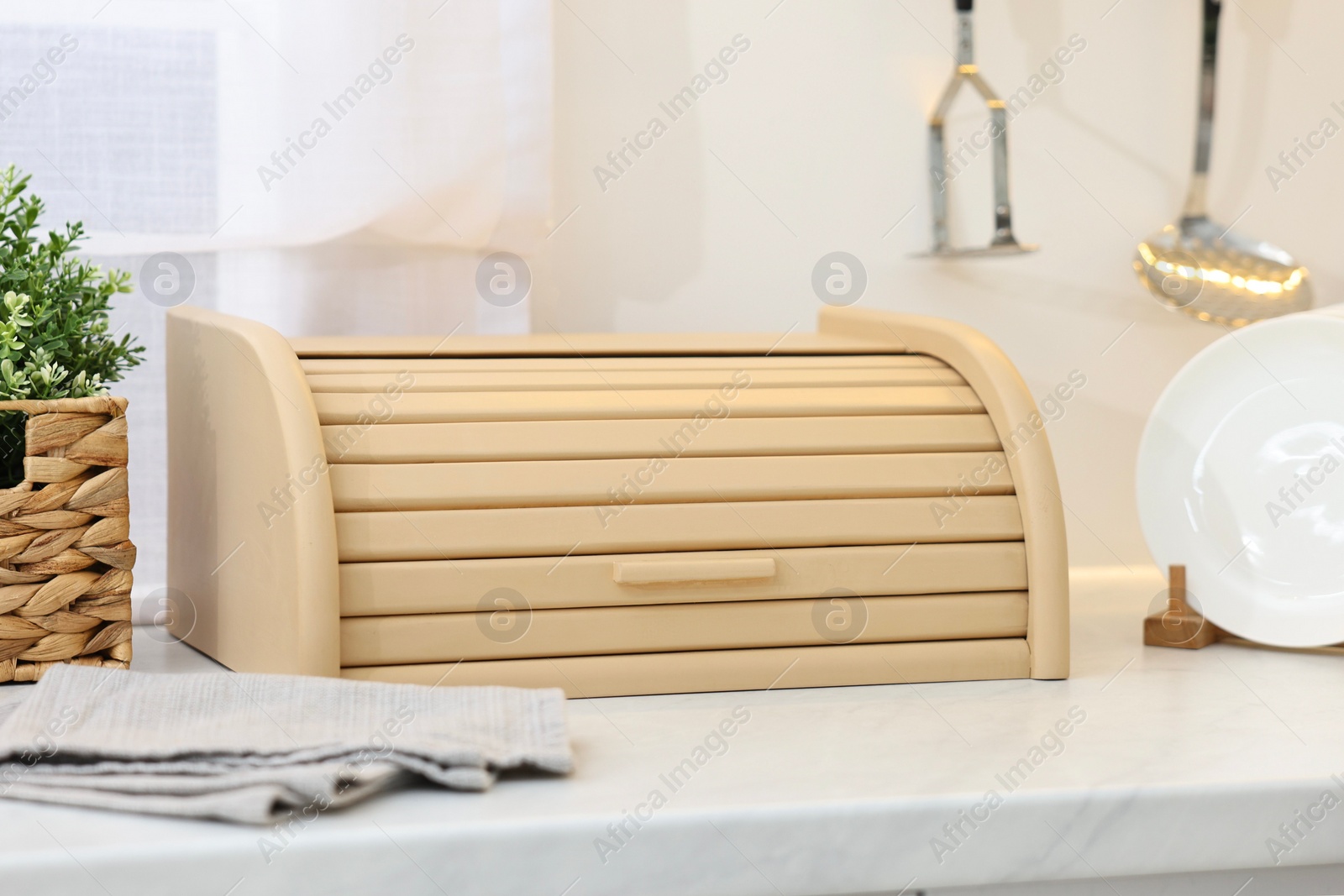 Photo of Wooden bread box, houseplant and plates on white marble countertop in kitchen