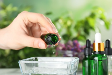 Photo of Woman dripping essential oil into bowl on table, closeup