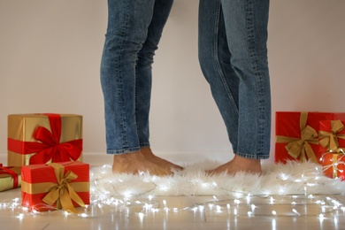 Photo of Young couple standing on rug near Christmas lights and gift boxes, closeup