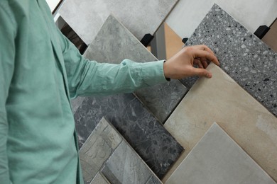 Photo of Man choosing tile among different samples in store, closeup