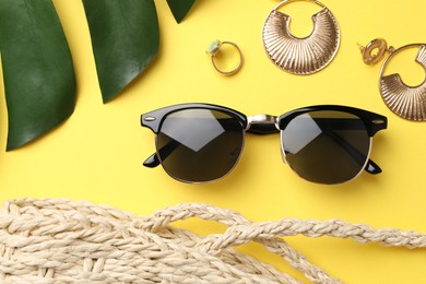 Photo of New stylish sunglasses, jewelry and bag on yellow background, flat lay
