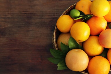 Wicker basket with different citrus fruits and leaves on wooden table, top view. Space for text