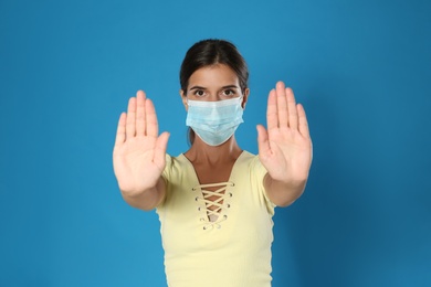 Photo of Woman in protective mask showing stop gesture on blue background. Prevent spreading of coronavirus