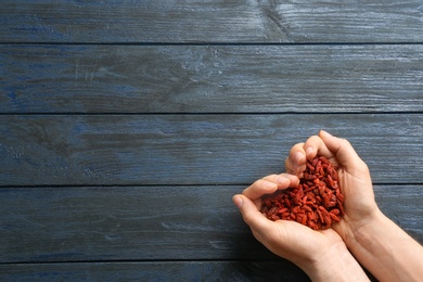 Woman holding goji berries on blue wooden background, top view with space for text. Heart health