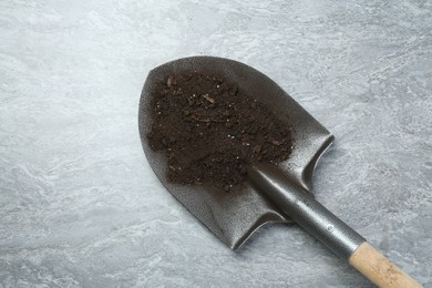 Photo of Metal shovel with fertile soil on gray textured surface, top view. Space for text