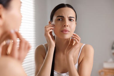 Woman with dry skin looking at mirror in bathroom