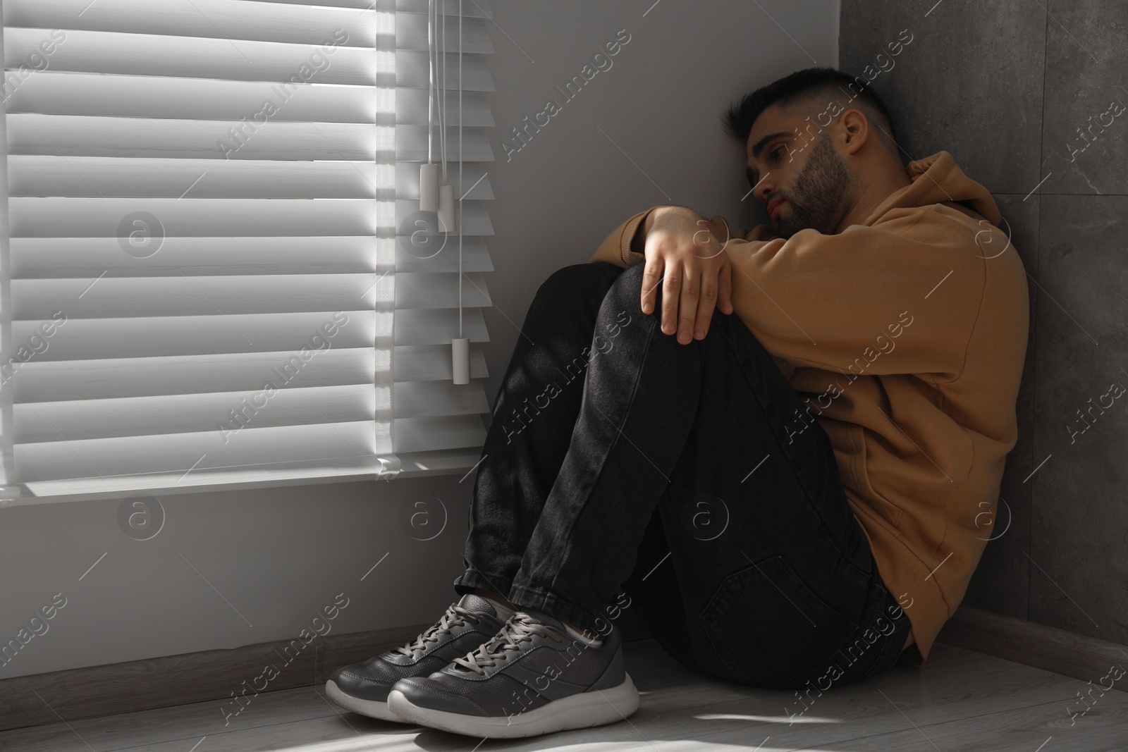 Photo of Sad man sitting on floor near window. Space for text