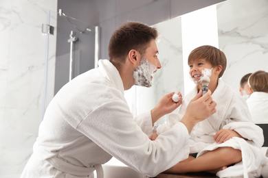 Dad applying shaving foam onto son's face in bathroom