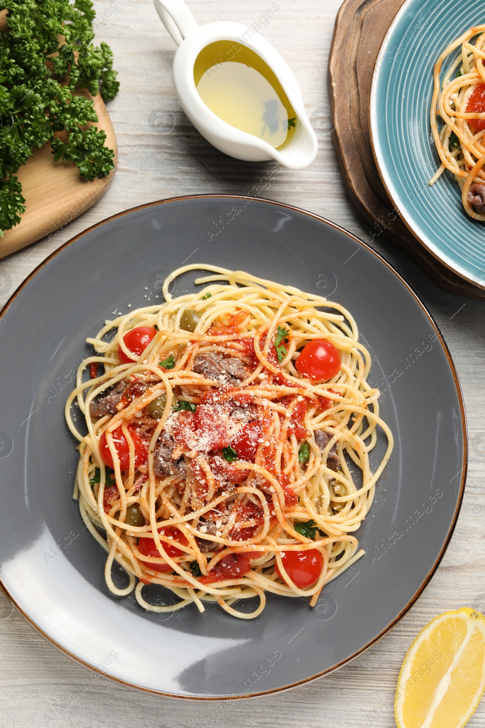 Photo of Delicious pasta with anchovies, tomatoes and parmesan cheese served on white wooden table, flat lay