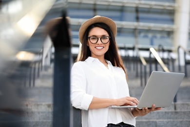 Photo of Beautiful woman with glasses using laptop on city street