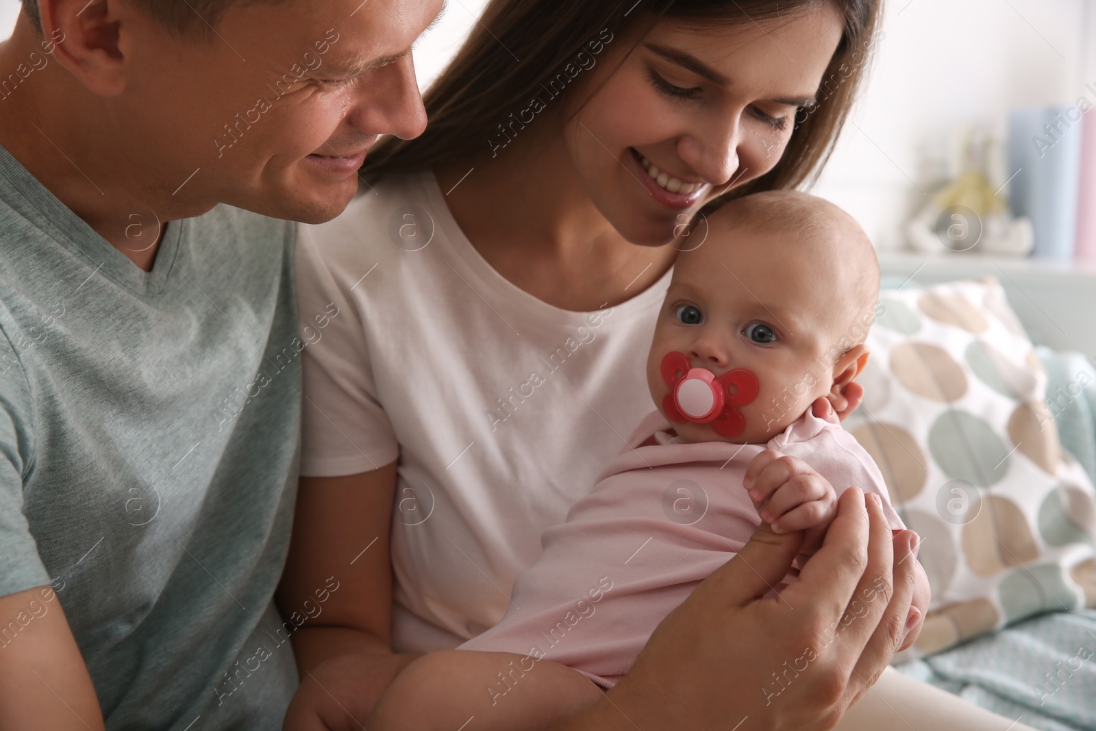 Photo of Happy couple holding their cute little baby with pacifier at home