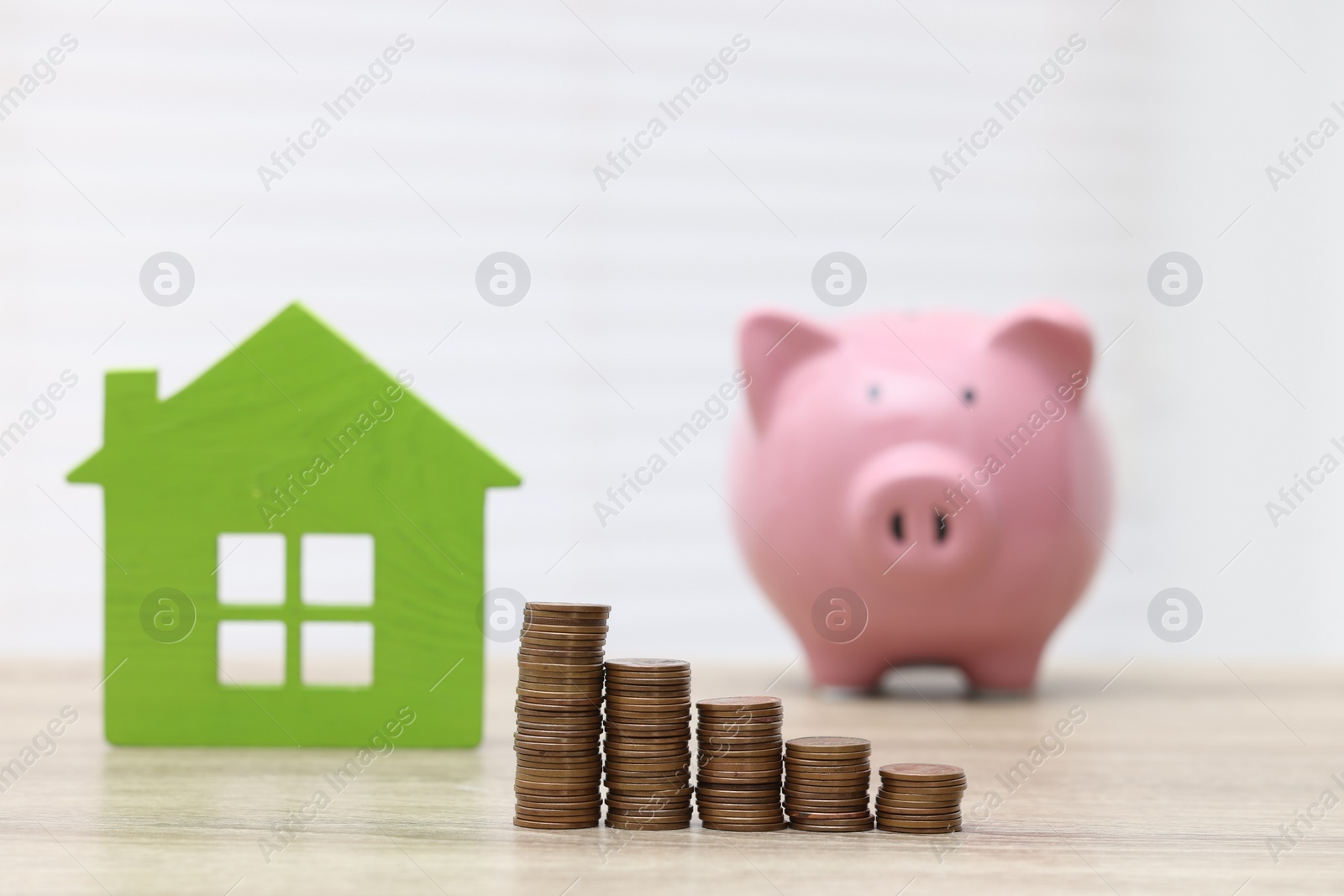 Photo of House model, piggy bank and stacked coins on wooden table, selective focus