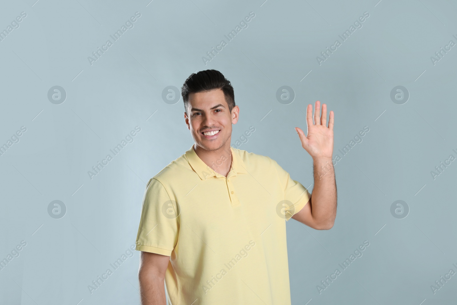 Photo of Cheerful man waving to say hello on grey background