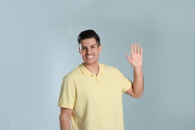 Photo of Cheerful man waving to say hello on grey background