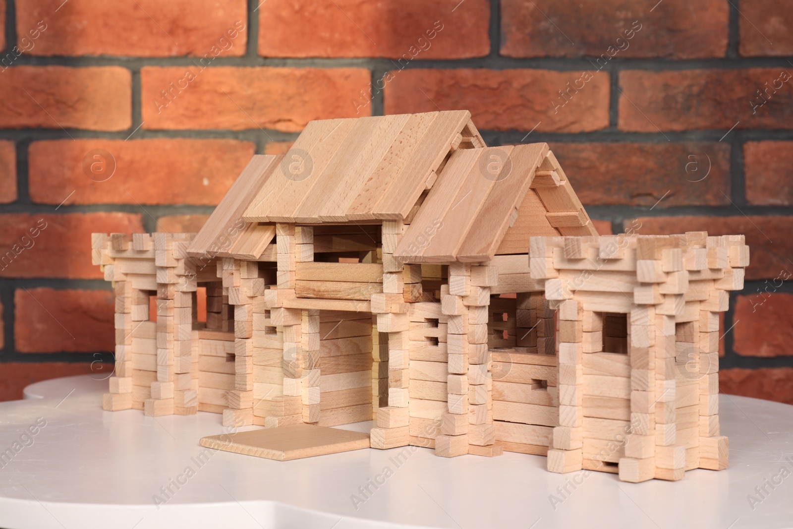 Photo of Wooden castle on white table near brick wall. Children's toy