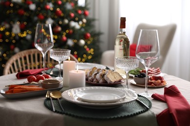 Photo of Christmas table setting with burning candles, appetizers and dishware indoors