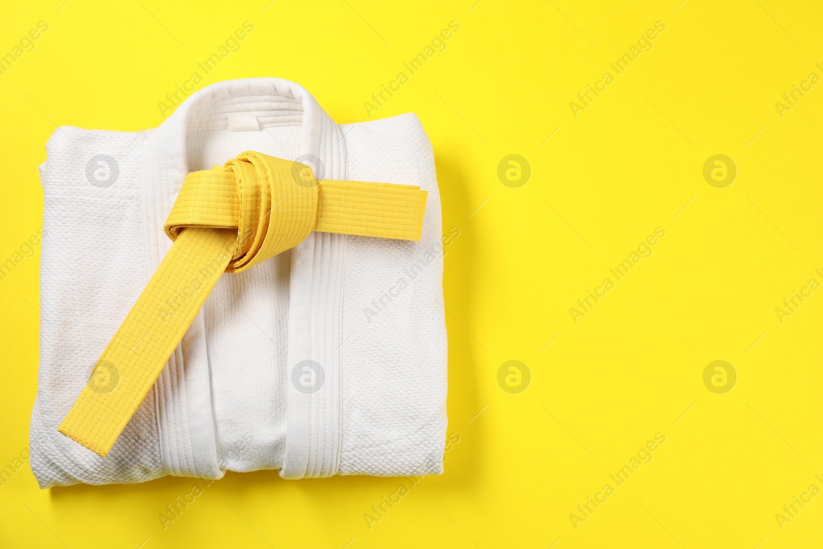 Photo of Karate belt and white kimono on yellow background, top view. Space for text