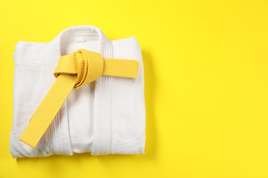 Karate belt and white kimono on yellow background, top view. Space for text