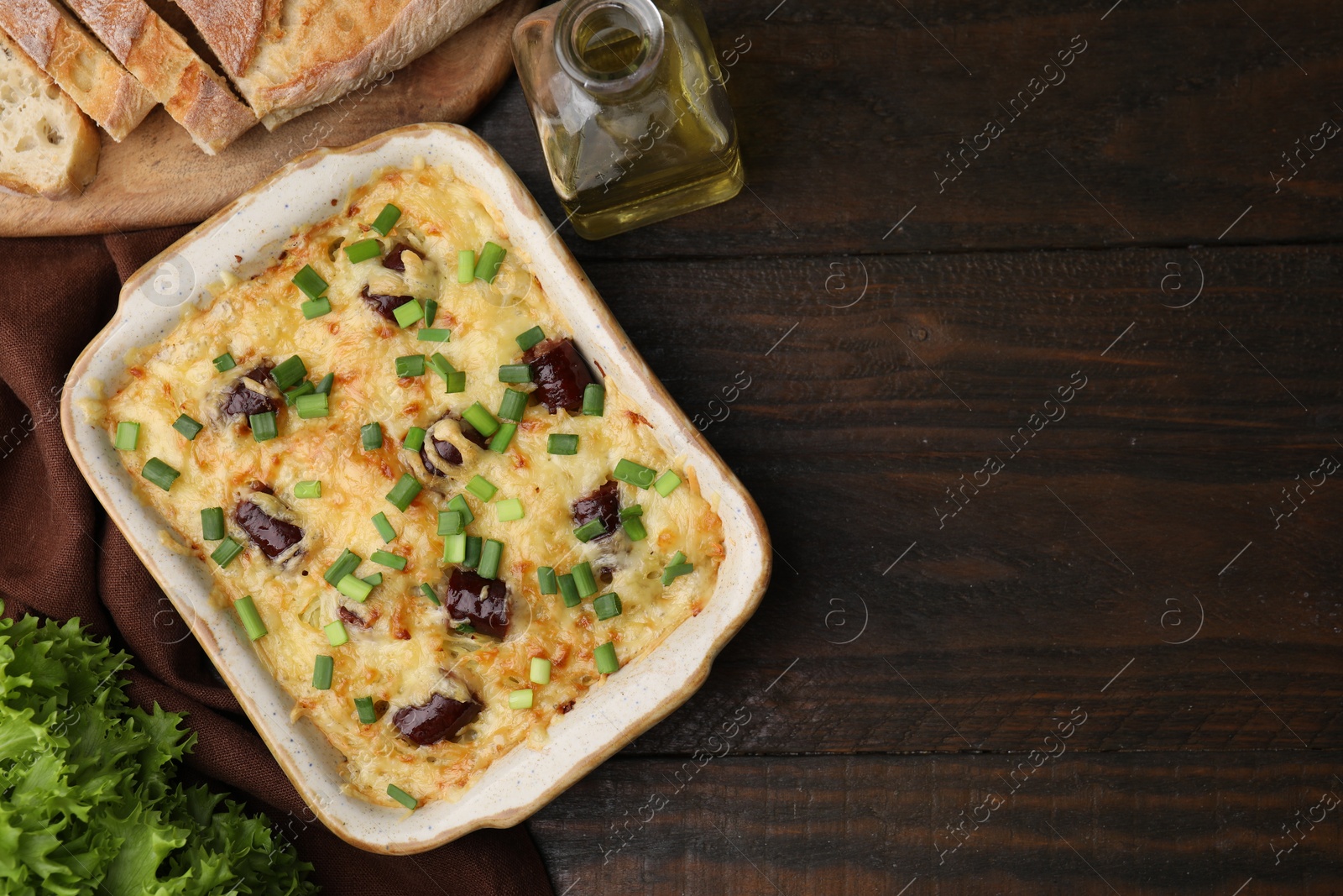 Photo of Tasty sausage casserole with green onions in baking dish on wooden table, flat lay. Space for text