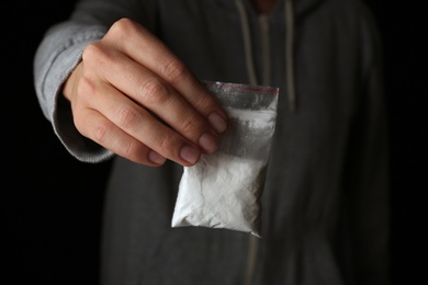 Photo of Drug dealer holding bag with cocaine on black background, closeup